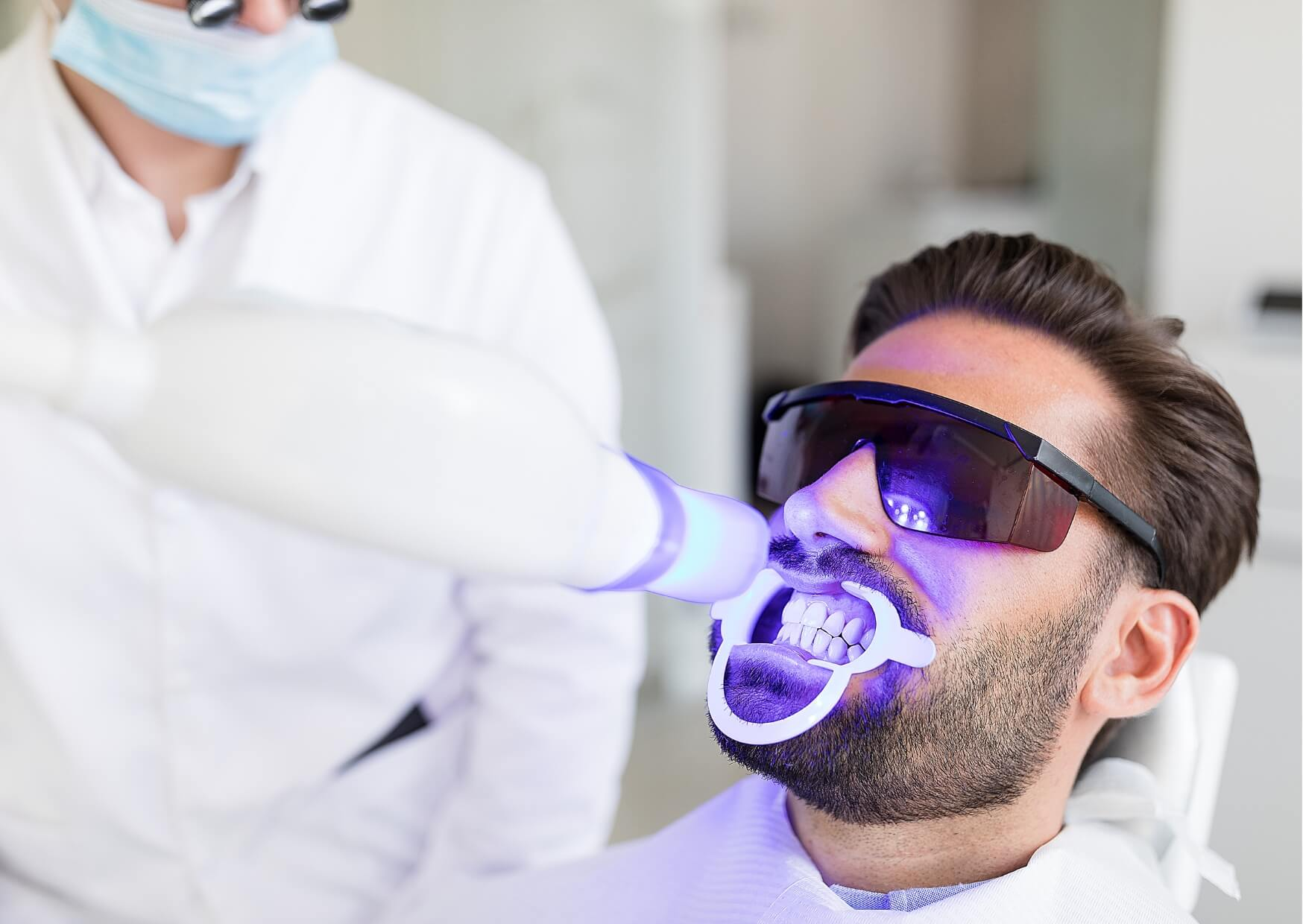 Patient undergoing professional teeth whitening treatment with a dental curing light, highlighting one of the available teeth whitening options for a brighter smile.